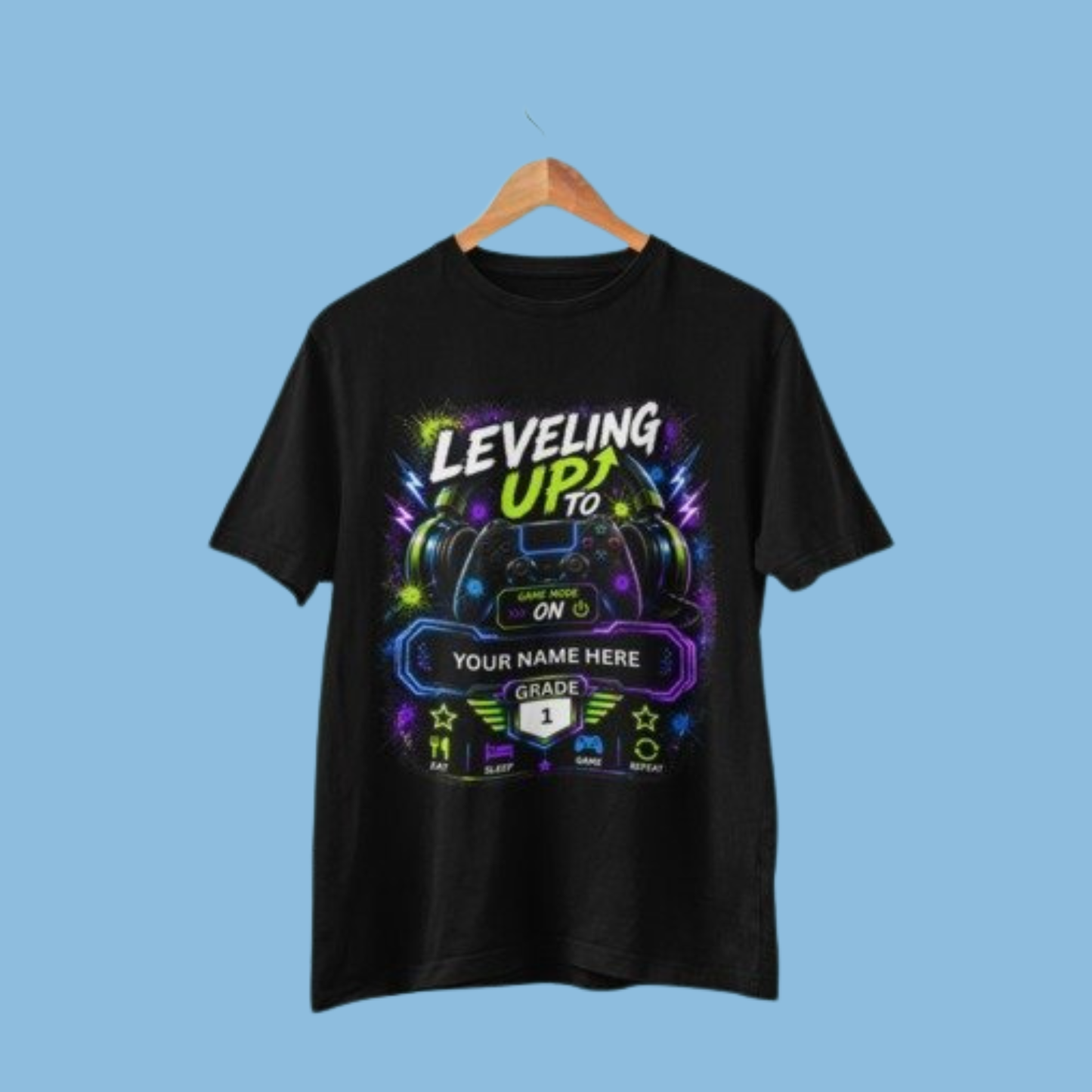 A black short-sleeve t-shirt hanging on a wooden hanger against a solid light blue background. The shirt features a colorful graphic print with gaming-themed text reading 'LEVELING UP TO YOUR NAME HERE' and 'GRADE 1' on a black banner.