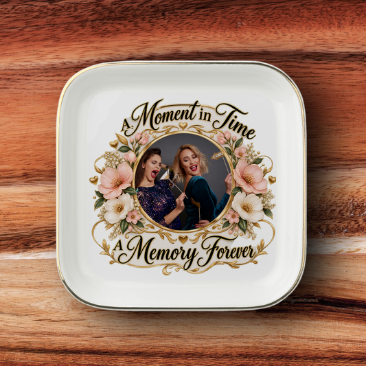 A square white ceramic keepsake plate with rounded corners, featuring a custom photo of two women framed by pink flowers and gold decorative scrollwork, with the text 'A Moment in Time' and 'A Memory Forever', set against a wooden background.